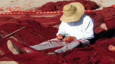 Visser met hoed repareert rode visnetten, Essaouira, Marokko