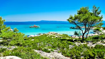Een panorama van Portokali (Orange) Beach in Sithonia, Halkidiki, Griekenland met een toeristische schip. De oorspronkelijke naam is Kavourotripes