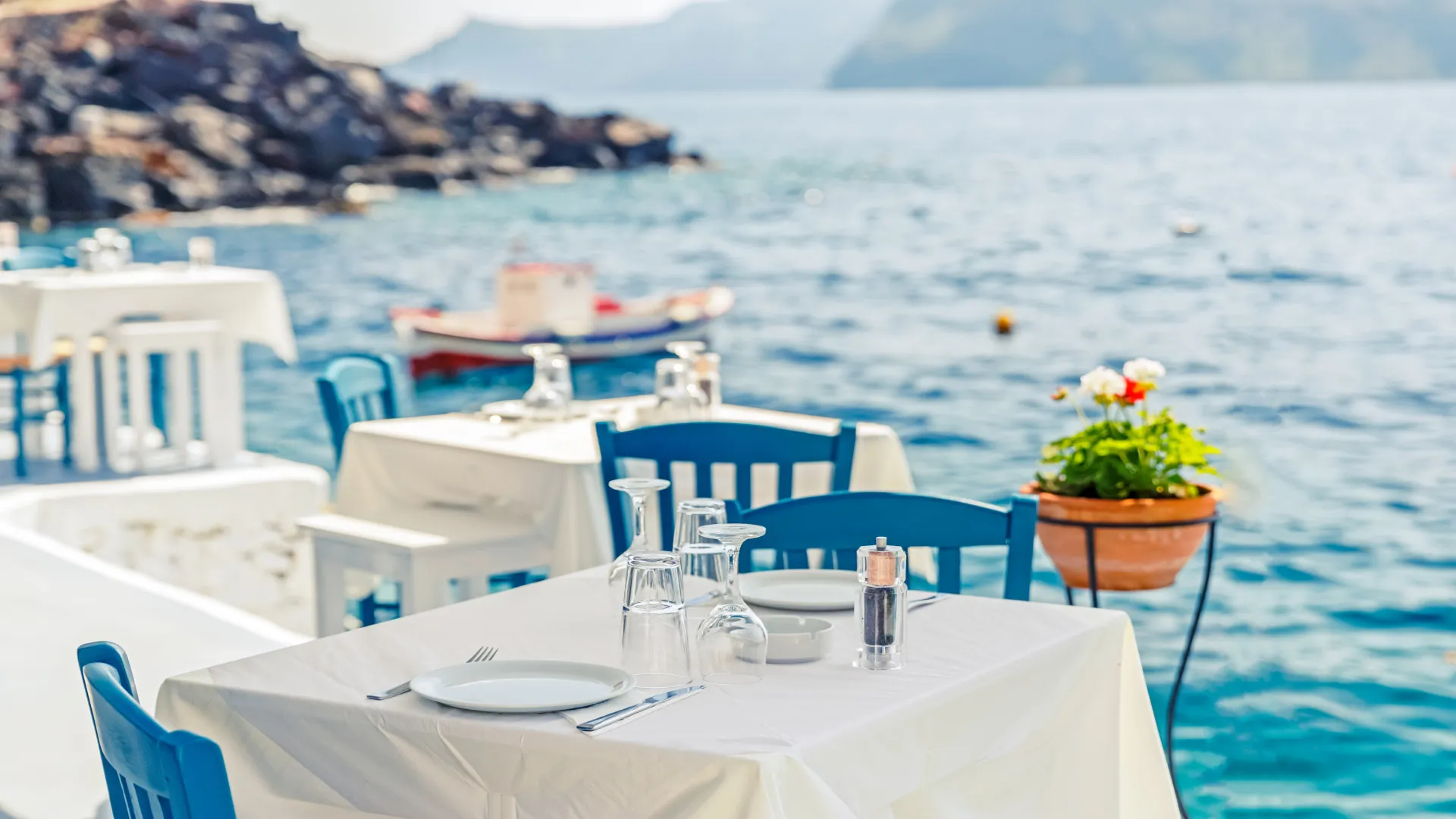 Gedekte tafel op terras van restaurant aan het water met uitzicht op zee en de dijk van Oia dorp, Santorini, Griekenland 