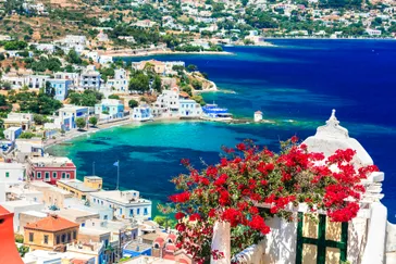 Leros - Agia Marina - blauw water, heuvels met groene bomen en witte huisjes, rode bloemen op de voorgrond
