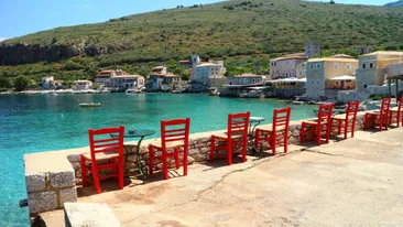 Terras met rij rode stoelen kijkt uit over de blauwe zee en stenen huizen in Limeni, Mani, Peloponnesos, Griekenland
