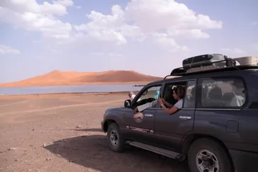 Auto bij Merzouga met duinen op achtergrond, Marokko