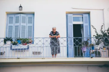 Griekenland oud vrouwtje op balkon blauwe luiken
