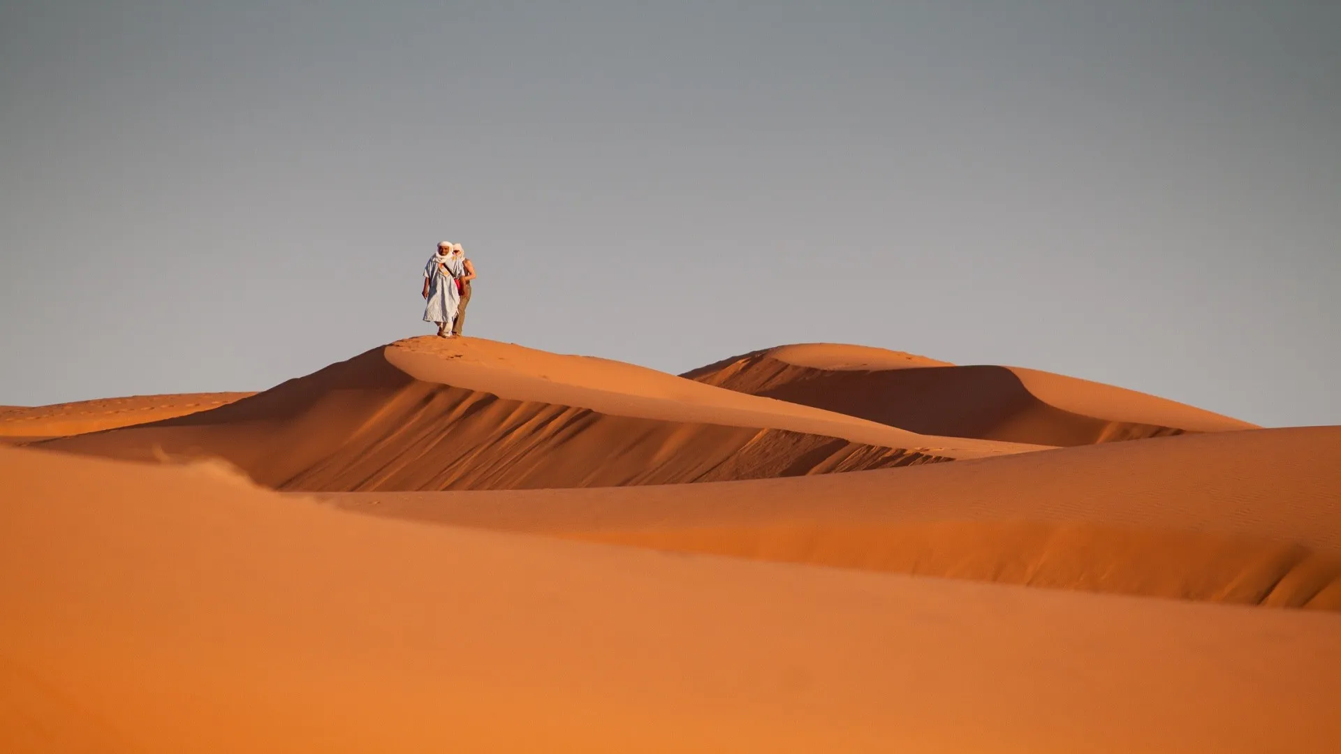 Man lopend in woestijn op oranje zandduin, Zuid Marokko