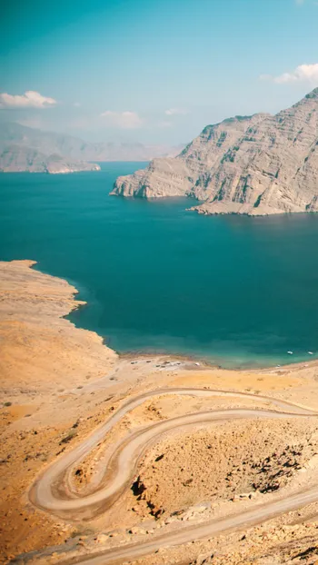 Thema fly-drive Oman, slingerende weg in de bergen met zee