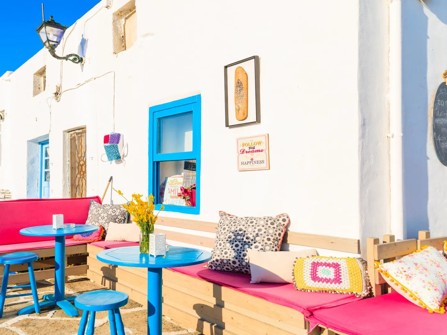 Naoussa terras, Paros, Griekenland, blauwe tafeltjes, rose kussens op de bank en wit gebouw